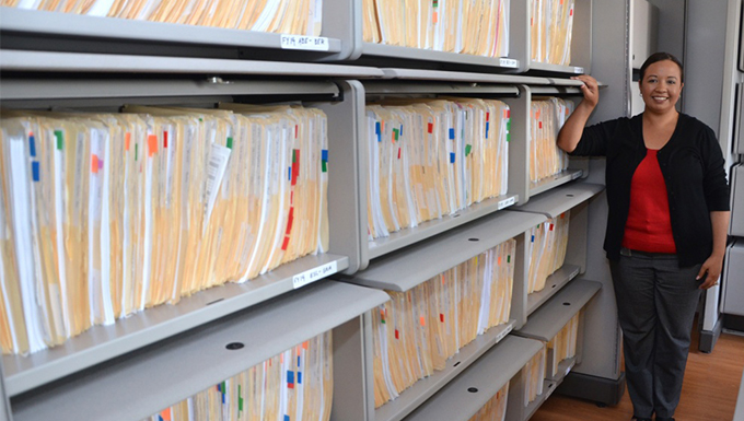 A woman standing next to filing cabinets. 