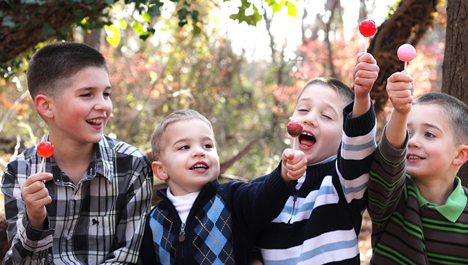 A group of children sitting together outside eating candy suckers.