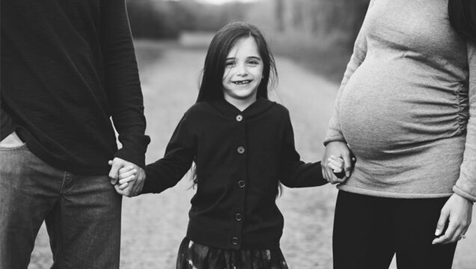A little girl touching her pregnant mother and father.
